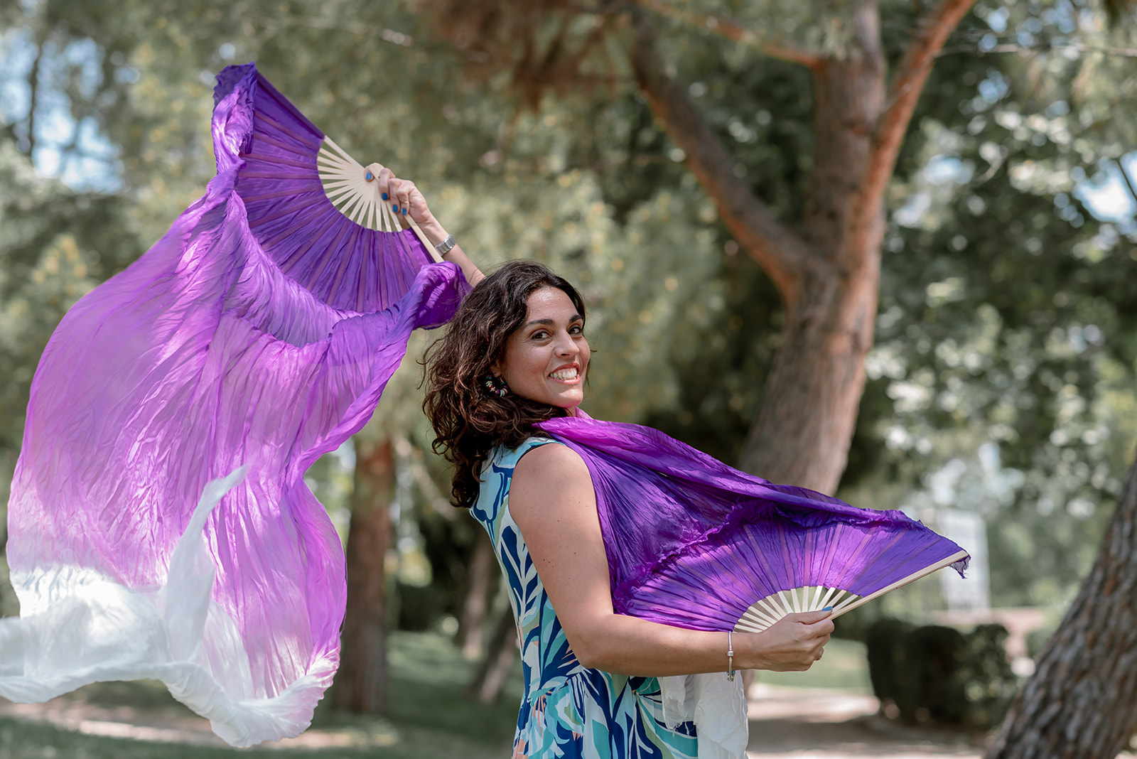 Mujer usando dos abanicos morados y sonriendo a cámara